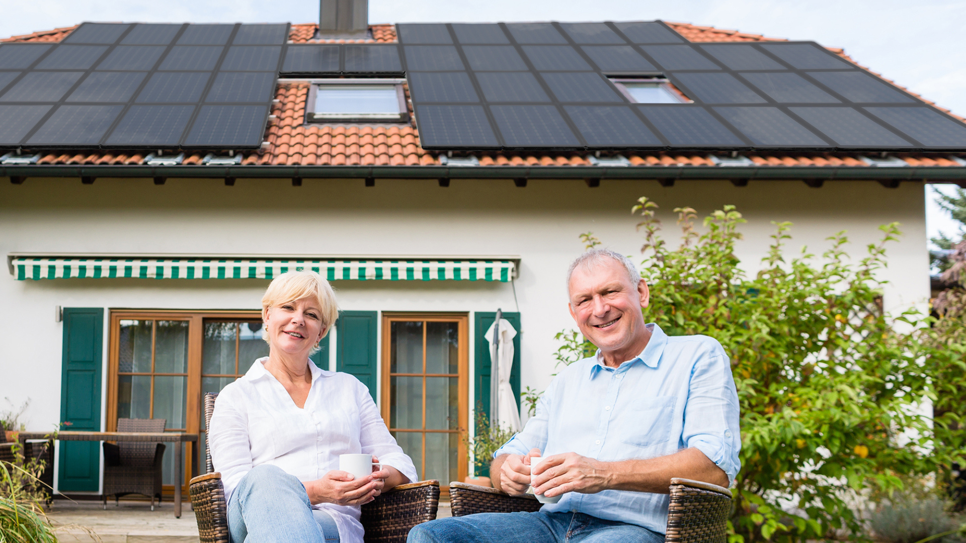 Eine Frau und ein Mann die im Garten Ihres Hauses sitzen. Im Hintergrund sieht man Ihr Haus mit einer verbauten Photovoltaikanlage